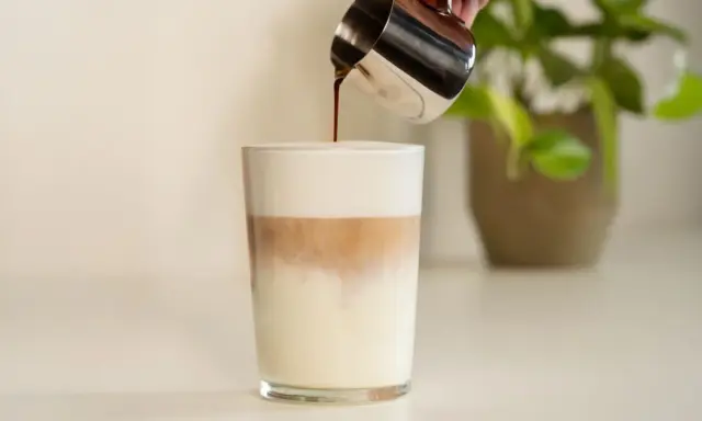 Espresso wird in ein Glas mit Milch und Milchschaum gegossen. Ein perfektes Latte Macchiato Rezept.