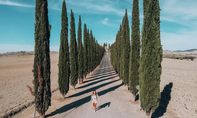Viale di cipressi nel Val d'Orcia, un'icona da vedere in 3 giorni. Una donna cammina lungo la strada sterrata.