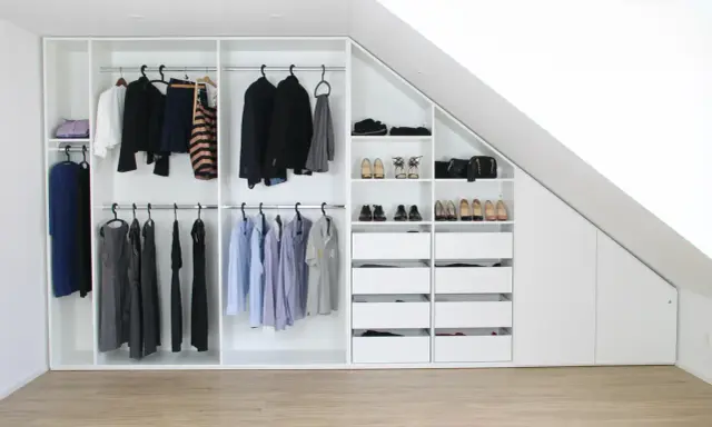 Ein maßgefertigter Kleiderschrank bauen, der sich perfekt in die Dachschräge einfügt. Ordentlich sortierte Kleidung und Schuhe.