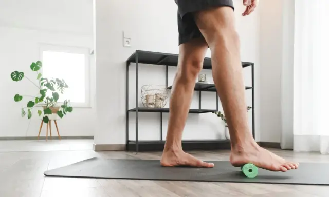 Mann rollt mit einem kleinen grünen Ball unter dem Fuß, um Plantarfasziitis-Hausmittel anzuwenden.