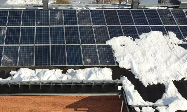 Snö täcker delar av solpanelerna på ett tak. Snart är det dags att skotta solpaneler för att fånga solens energi igen.