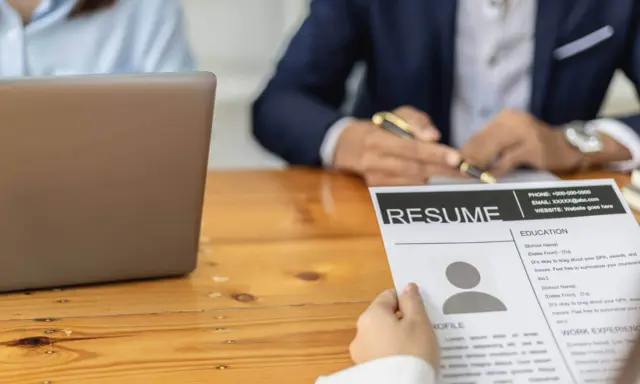 Osoba przegląda CV, na którym widnieje sekcja "Umiejętności twarde". Obok leży laptop.