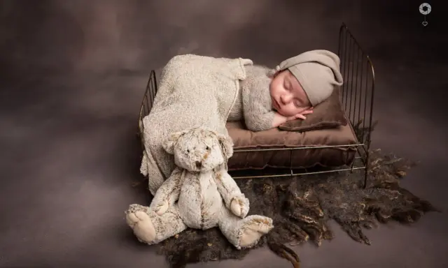 Dolce bimbo appena nato dorme sereno in una culla con un orsacchiotto. Foto bimbi appena nati.