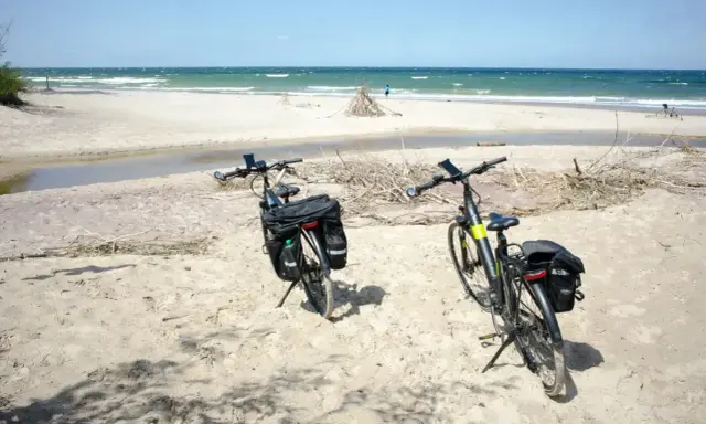 Dwa rowery z sakwami na piaszczystej plaży, gotowe na odkrywanie płaskich tras rowerowych nad morzem.