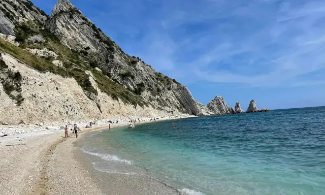 Spiaggia della Riviera del Conero con bambini che giocano e si bagnano, scogliere bianche e mare azzurro.