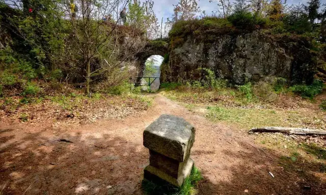 Kamienny postument przed łukiem w fort karola. Ścieżka prowadzi przez zarośla do zabytkowej budowli.