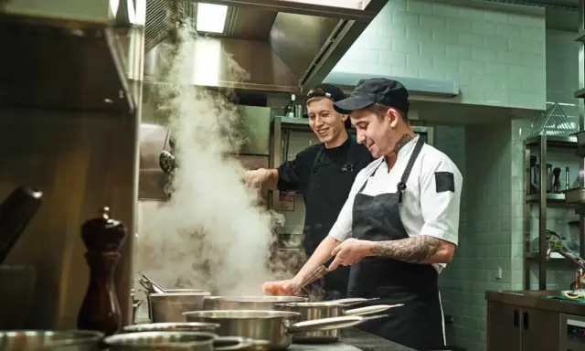Deux chefs travaillent dans une cuisine de restaurant, respectant la norme de qualité. Vapeur s'échappant des casseroles.
