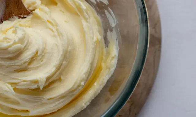 Une cuillère en bois mélange une crème au beurre traditionnelle onctueuse dans un bol en verre.