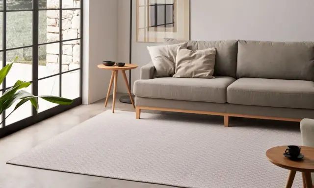 Un salón moderno con un sofá gris, una alfombra de diseño y una mesa auxiliar.