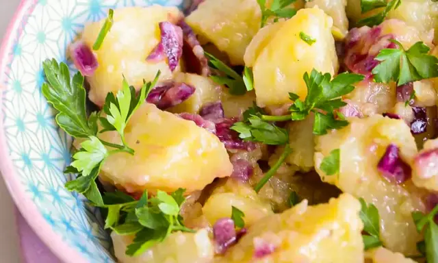 Salade de pomme de terre crémeuse avec des oignons rouges et du persil frais, servie dans un bol décoratif.