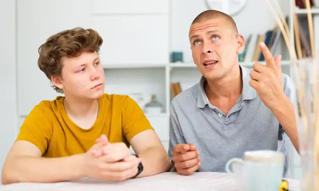 Ojciec tłumaczy synowi, jak rozmawiać z nastolatkiem, używając gestów. Chłopak słucha uważnie.