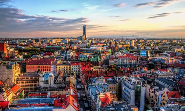 Widok na Wrocław, największe miasto zachodniej Polski, z dominującym wieżowcem Sky Tower. Słońce zachodzi nad kolorowymi dachami kamienic.