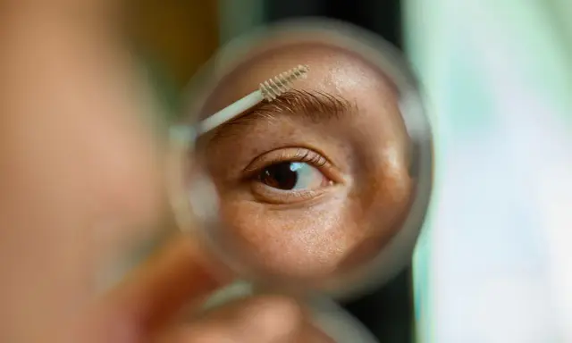 Gros plan sur un œil et un sourcil, une brosse à sourcils est utilisée pour les coiffer. La question est : est ce que les sourcils repoussent ?