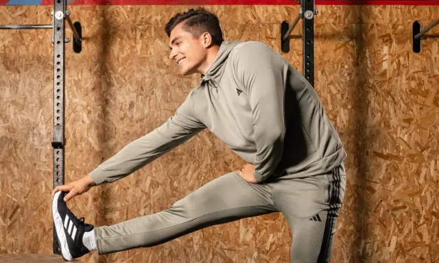 Ein Mann in Trainingskleidung macht dynamisches Dehnen vor einer Holzwand.
