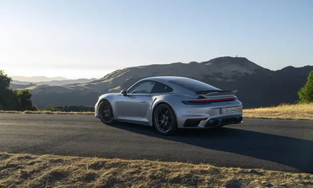 Silberner Porsche 911 Turbo S, ein Sondermodell 2023, parkt auf einer Bergstraße mit sanften Hügeln im Hintergrund.