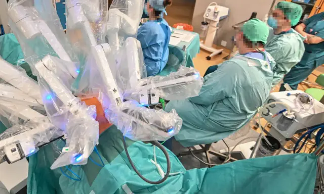 Chirurdzy w zielonych fartuchach prowadzą operację prostaty da Vinci. Robotyczne ramiona systemu są widoczne, pokryte sterylnymi osłonami.