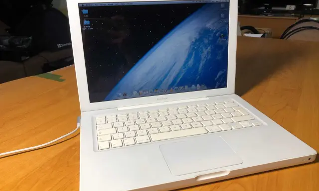 Biały, pierwszy MacBook z widokiem Ziemi na ekranie, stoi na drewnianym stole.