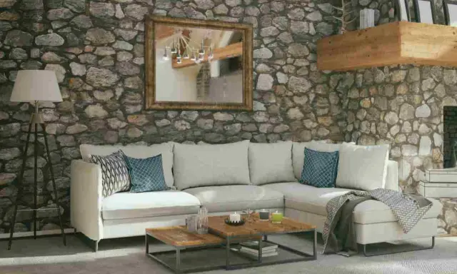 Soggiorno accogliente con pareti in pietra grezza, divano bianco, tavolini in legno e specchio dorato. Ottime idee pareti in pietra per un ambiente rustico.