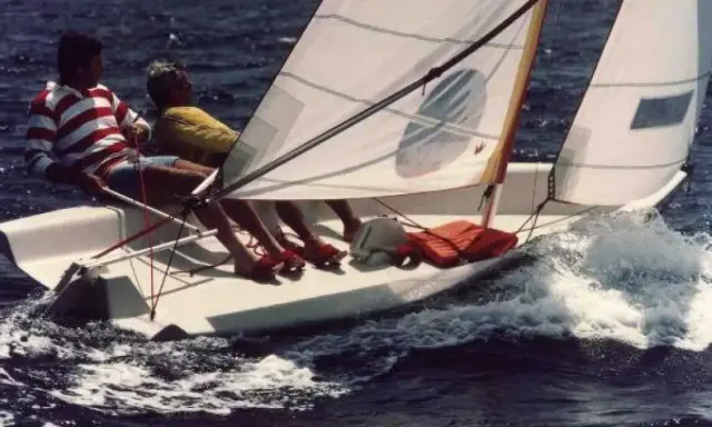 Deux personnes naviguent sur un dériveur Wizz, le bateau fend les vagues dans une joyeuse course.