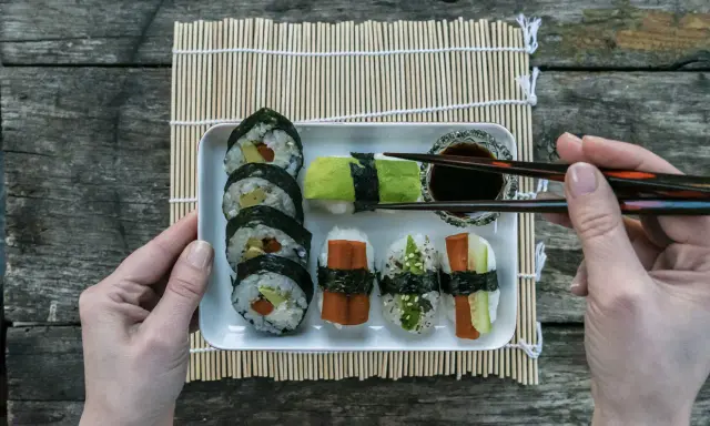 En bricka med olika sorters sushi, perfekt för ett enkelt sushi recept. En hand håller ätpinnar redo att plocka upp en bit.