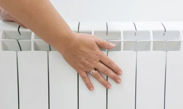 Main posée sur un radiateur électrique blanc, vérifiant la température hors gel.