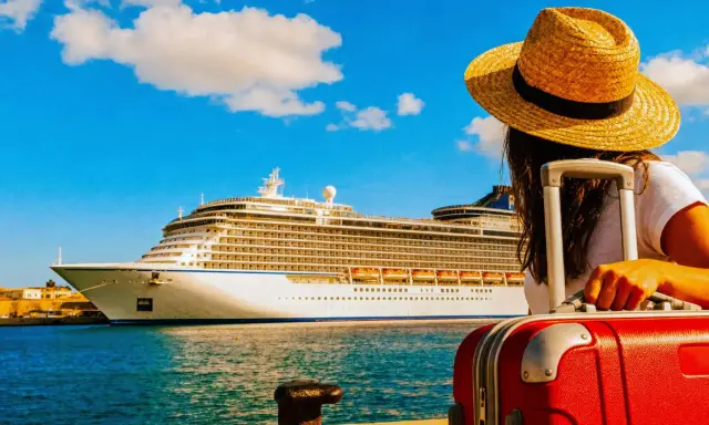 Donna con valigia rossa e cappello di paglia guarda una grande nave da crociera. Forse si paga per scendere dalla crociera.
