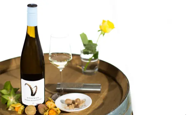 Flasche Gelber Muskateller Wein, Glas, Sternfrucht, Physalis, Litschi und Muskatnuss auf einem Holzfass.