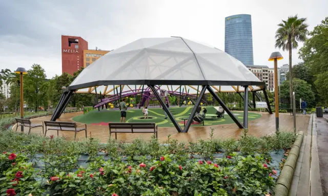 Modern playground under a geodesic dome in Parque Doña Casilda. Children play while parents relax on benches.
