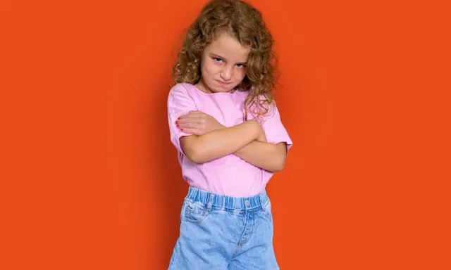 Niña con rizos, brazos cruzados y expresión de enfado. Podría representar la **depresión infantil** o simplemente un mal humor pasajero.