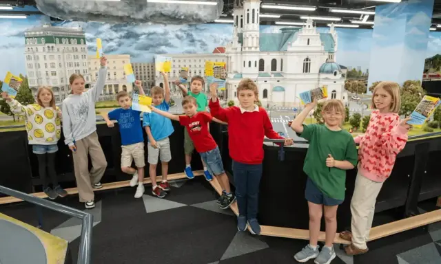 Dzieci z uśmiechem zwiedzają kolejkowo w Warszawie, trzymając w rękach foldery z atrakcjami.