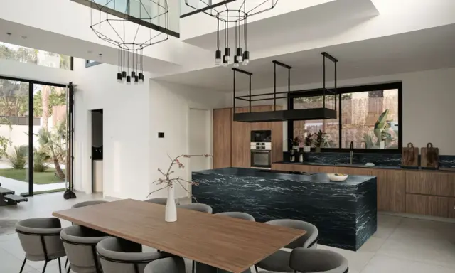 Nowoczesny salon z kuchnią otwartą: drewniane meble, czarna wyspa kuchenna, designerskie lampy i duży stół jadalniany.