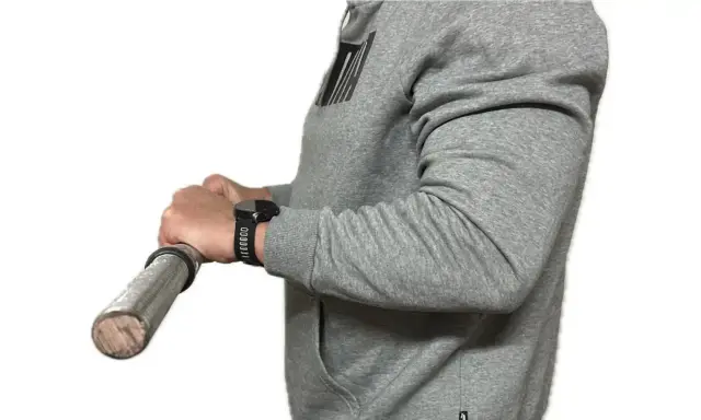 Person in grauem Hoodie macht einen Wrist Curl mit einer Hantel.