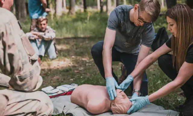 Uczestnicy kursu przetrwania ćwiczą resuscytację na fantomie w lesie.