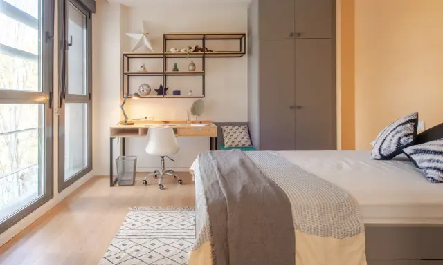 Habitación moderna en residencia San Bernardo Madrid. Escritorio, cama y armario gris. Ventanal con luz natural.