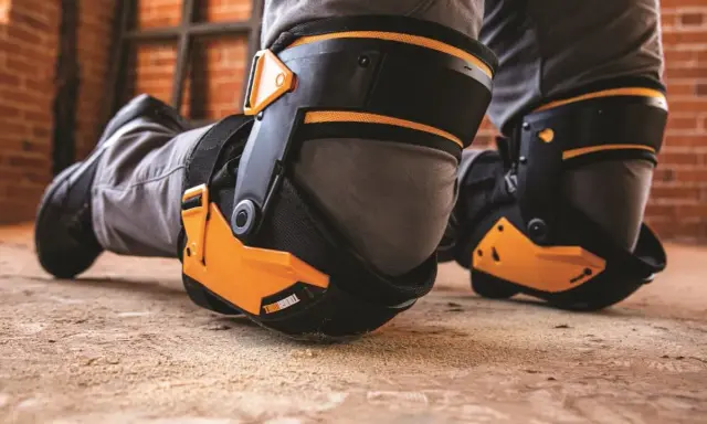 Protection des genoux pour éviter toute maladie professionnelle. Des genouillères robustes et orange protègent les genoux d'un travailleur sur un sol poussiéreux.