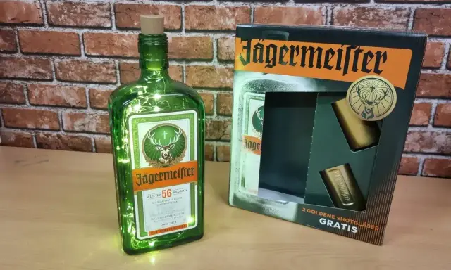 Butelka Jägermeistera z lampkami i zestawem kieliszków. Poznaj, jak smakuje jagermeister – ziołowy eliksir.
