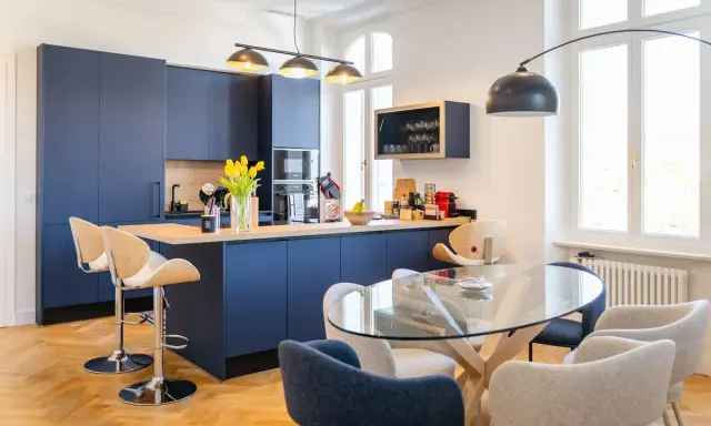 Élégante petite cuisine ouverte avec îlot central bleu marine, tabourets en bois et table en verre.