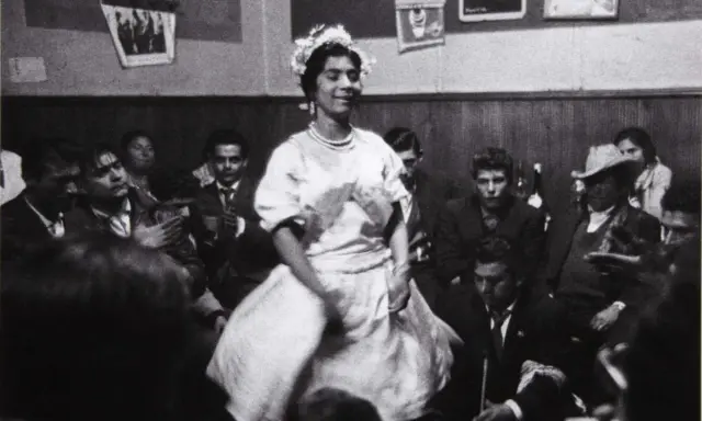 Una mujer con corona de flores baila en una celebración, rodeada de gente. Podría ser una boda gitana.