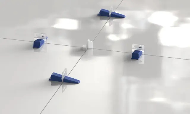 Sistema de nivelación de baldosas con cuñas azules y separadores blancos. La **matajunta desplazada** asegura una instalación perfecta.