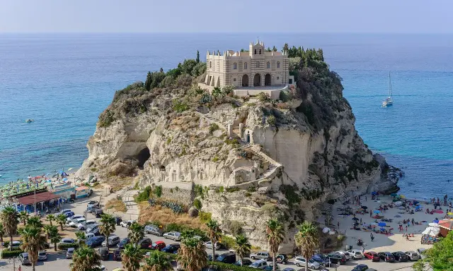 Santuario di Santa Maria dell'Isola a Tropea, regione Calabria, su uno sperone roccioso a picco sul mare azzurro, con spiaggia e palme.
