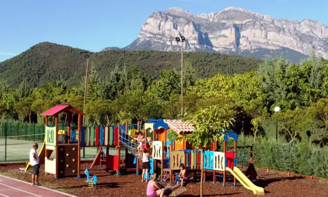 Parque infantil colorido en un camping de Huesca, con niños jugando y montañas imponentes al fondo.