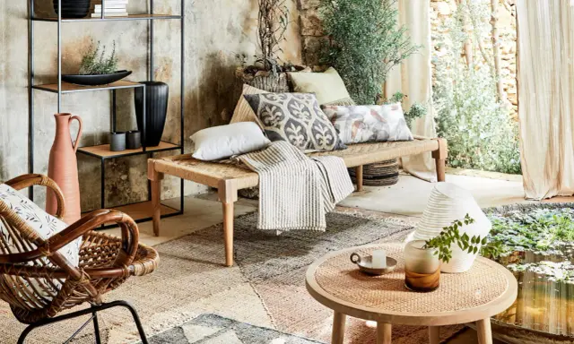 Un salon sans canapé, avec un banc tressé, un fauteuil en rotin, des coussins décoratifs et une étagère murale.