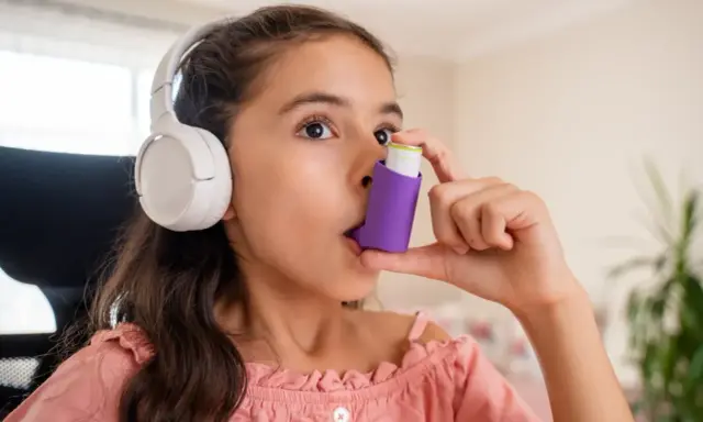 Mädchen mit Kopfhörern benutzt Inhalator gegen Asthma durch Stress.
