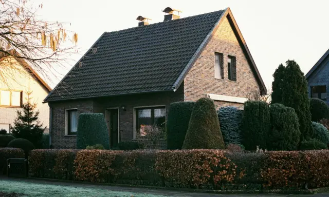 Ein gepflegtes Einfamilienhaus mit Ziegelfassade und dunklem Dach. Die Frage "wie viel kostet ein haus" wird durch die idyllische Szenerie aufgeworfen.