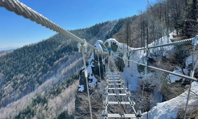 Zimowa przygoda na wiszącym moście nad przepaścią. Skalka pri Kremnici w śnieżnej odsłonie, z widokiem na zalesione zbocza.