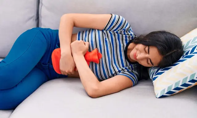 Joven con bolsa de agua caliente en el abdomen, aliviando el dolor de cólicos.