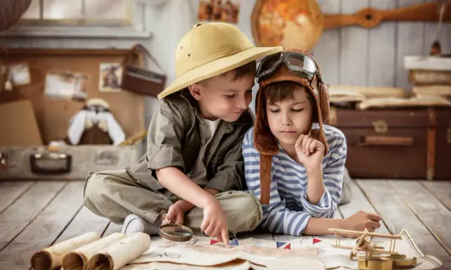 Dos niños planean una aventura en una casa rural para niños, con un mapa, lupa y sombrero de explorador.
