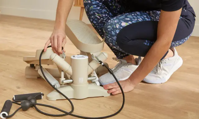 Osoba przygotowuje stepper skrętny czy prosty do ćwiczeń, podłączając linki oporowe.