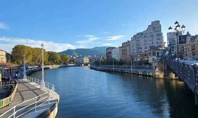Blick auf den Bilbao Fluss mit Gebäuden und einer Brücke im Hintergrund.
