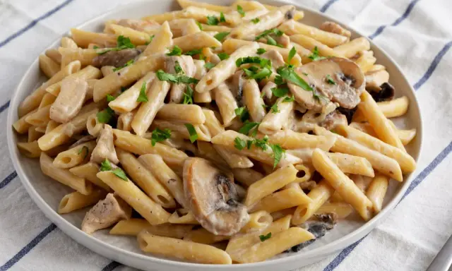 Penne z kurczakiem i pieczarkami w kremowym sosie, posypane natką pietruszki. Pyszne danie makaronowe.